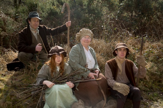 Four people in nineteenth century rural costume sitting on a bank
